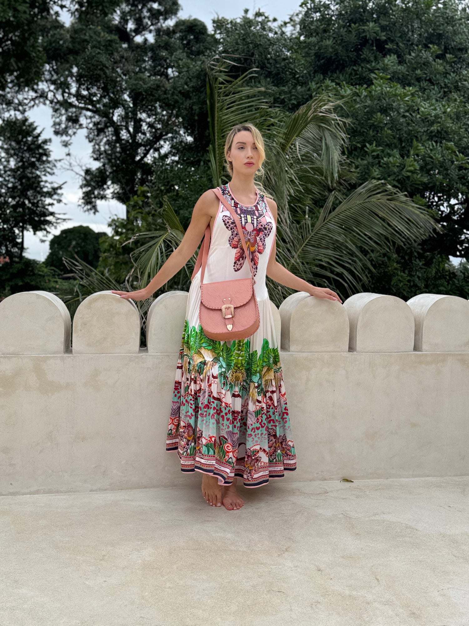 Perth luxury photography studio featuring a model in a vibrant dress holding a pink handbag by a rustic wall with plants