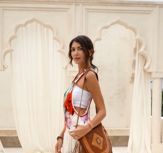 Stylish woman in white tube top and floral scarf standing before ornate arches and draped curtains