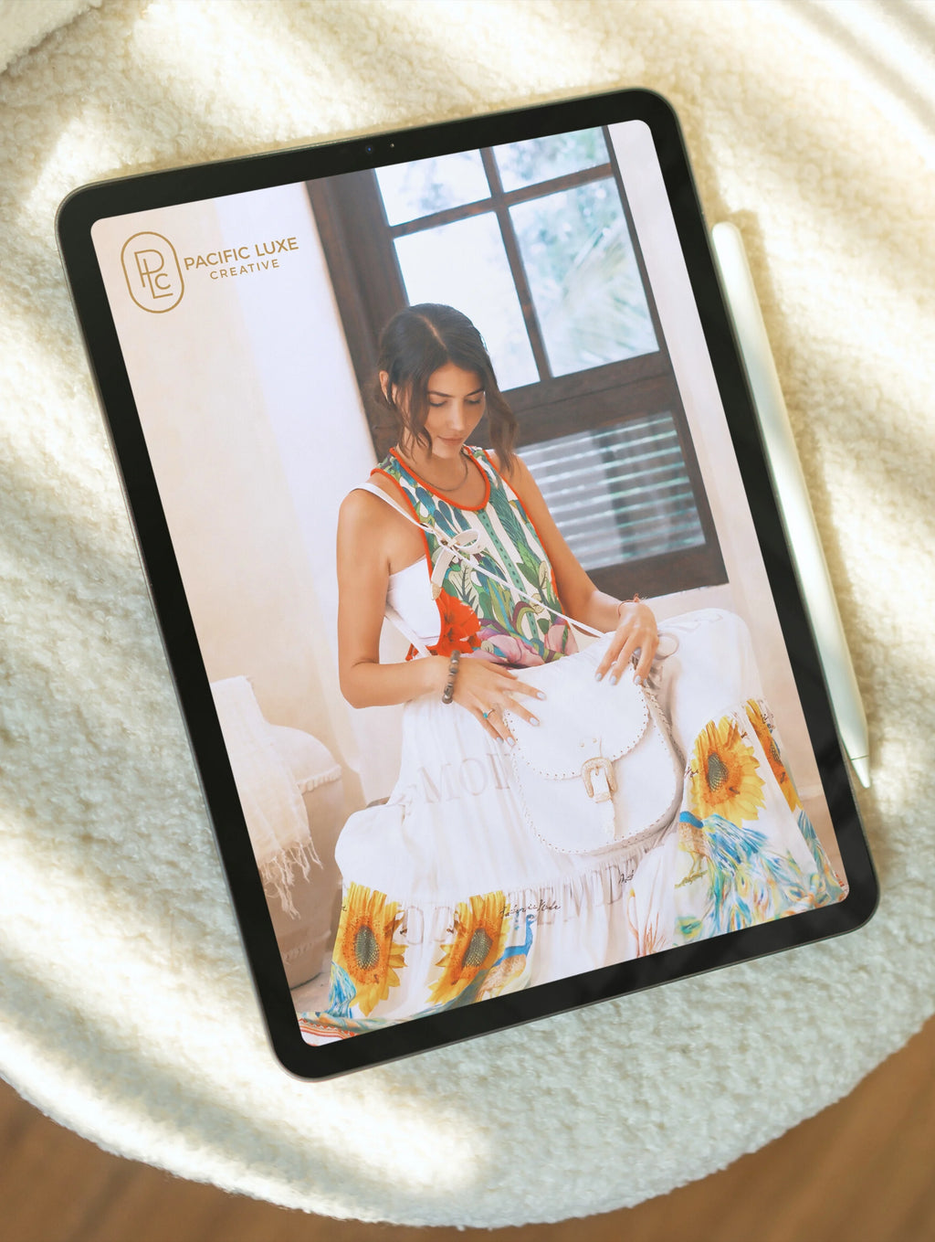 Pacific Luxe Creative brand photography tablet displaying a serene image of a woman holding a baby on a sunflower-patterned blanket, radiating Bali Paradise Shore glow.